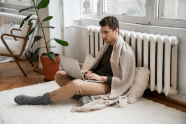 Un homme travaille avec son ordinateur assis contre son radiateur car il a froid. Il n'a pas un bon confort thermique au travail